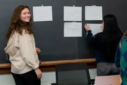 Two students place paper on a blackboard that describe aspects of education