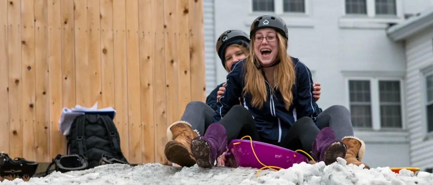 Two students about to sled down a small hill on the Biddeford Campus