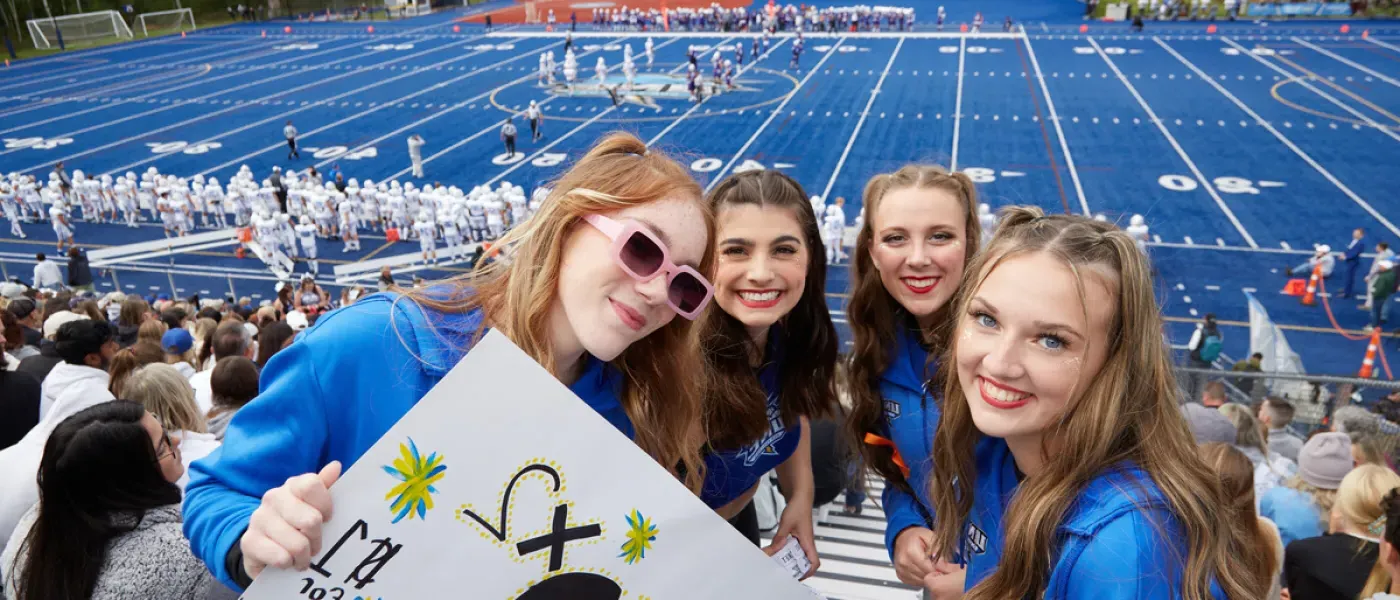 Four students cheering on the U N E football team at a home game